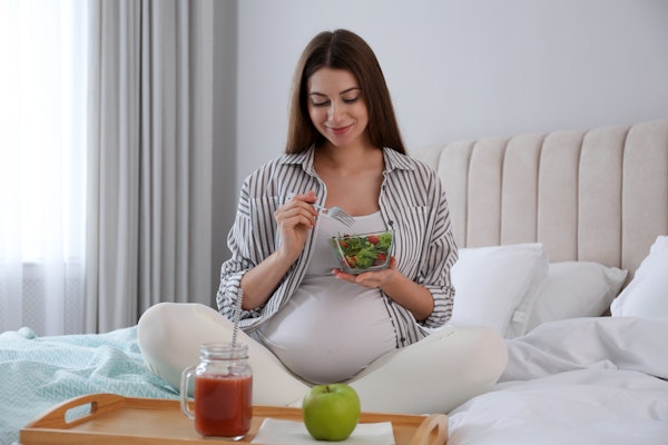 pregnant woman eating a salad on the bed