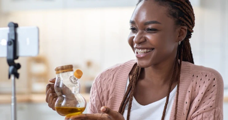 Woman recording a cooking video while holding a jar of olive oil, with fresh vegetables on the counter