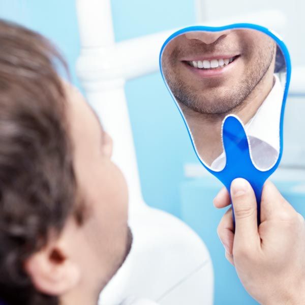 Older man smiling at reflection in handheld mirror