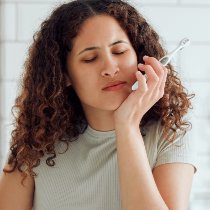 a woman in pain brushing teeth