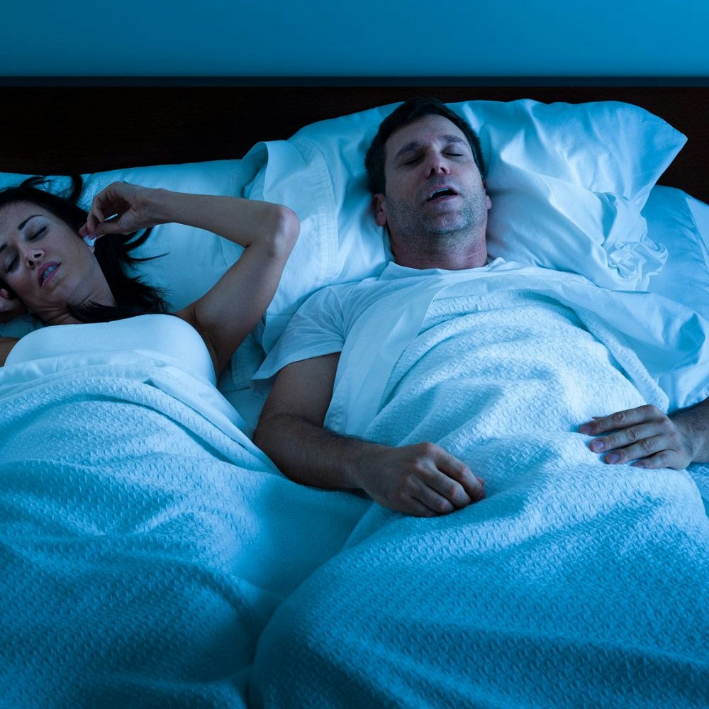 Man snoring in bed with woman covering ears next to him