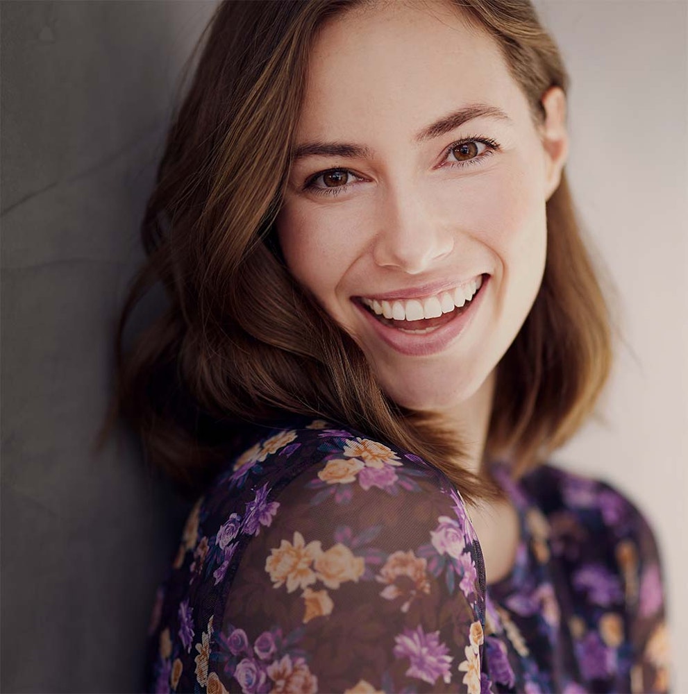 Young woman smiling while leaning on a concrete wall.