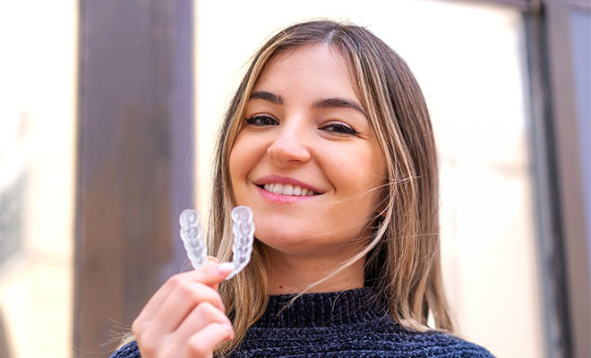 Woman smiling while holding invisalign