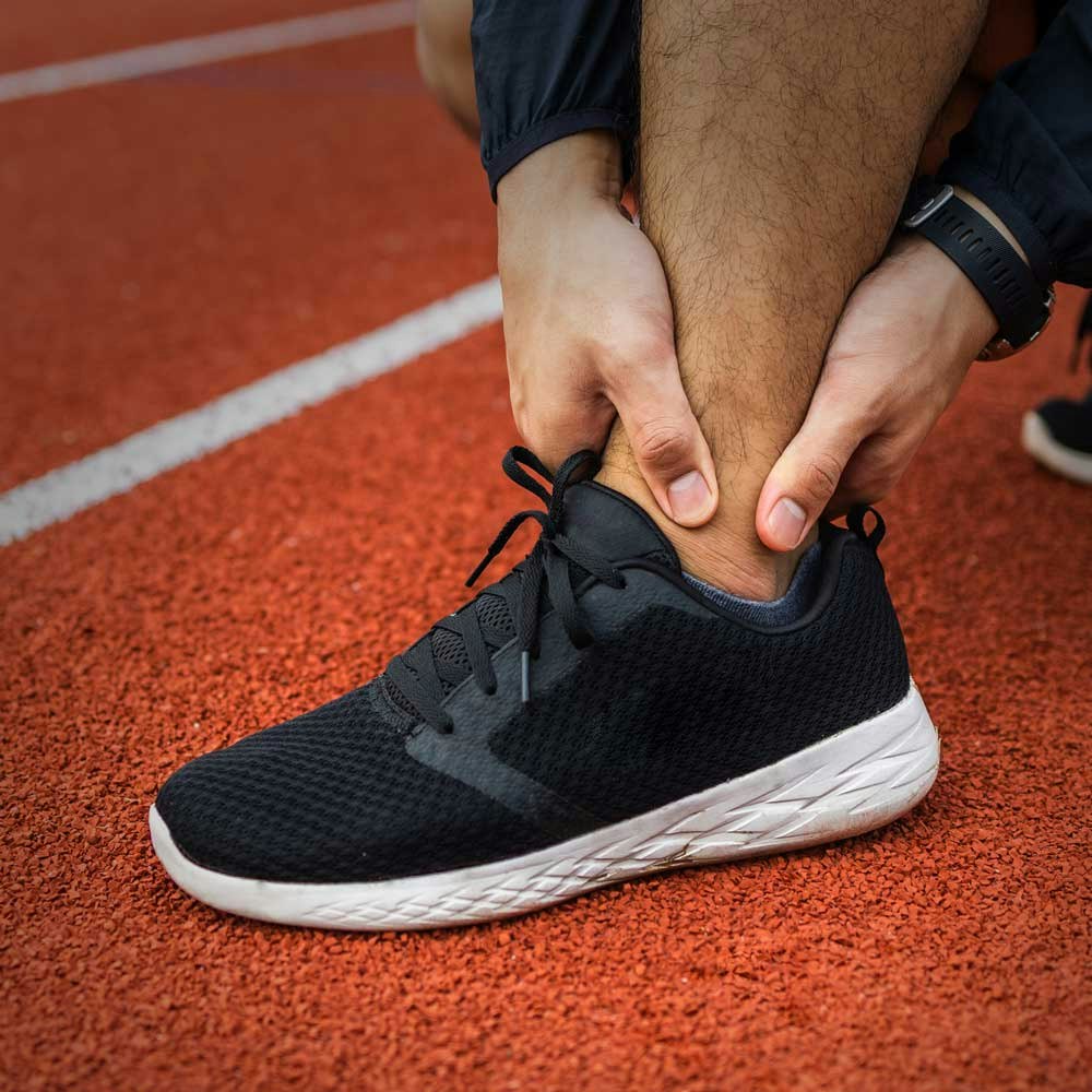 man on running track holding ankle in pain
