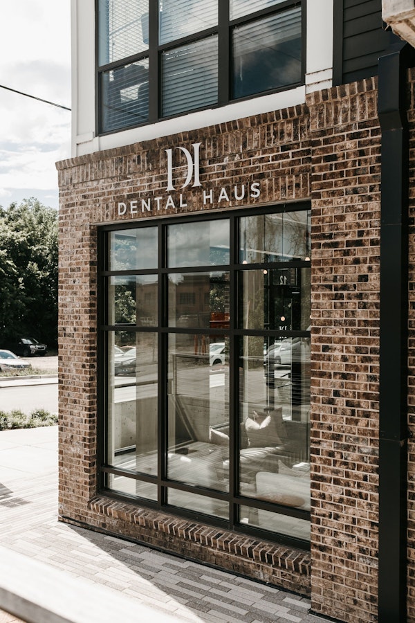 Exterior of Dental Haus storefront with brick facade, large black-framed windows, and white “DH Dental Haus” signage above the entrance