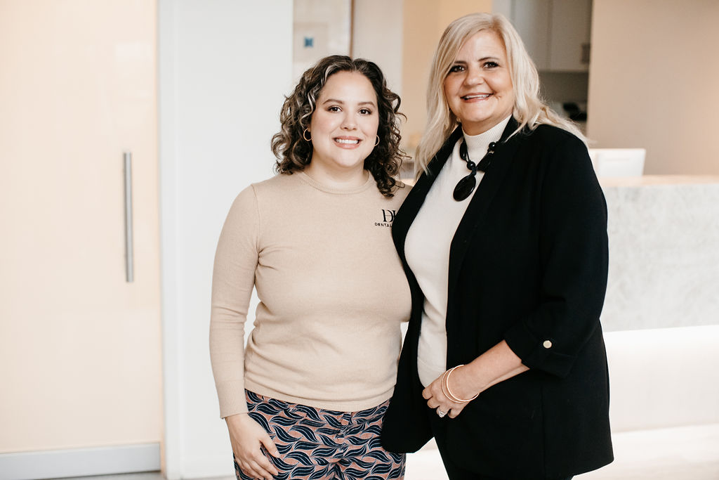Rebecca, Dental Haus office manager, standing in a black jacket beside a team member inside the Dental Haus reception area