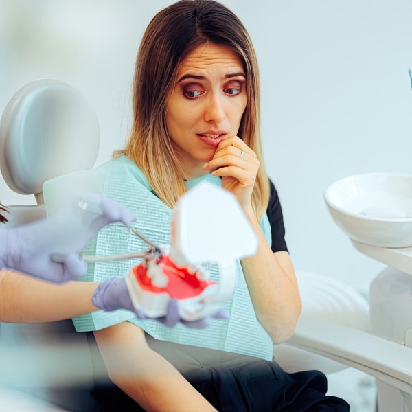 Woman looking fearfully at dentist who is demonstrating a tooth extraction on model