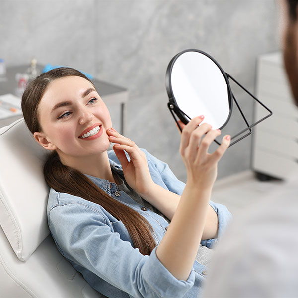 Young woman admiring her new smile in a mirror at the dental office