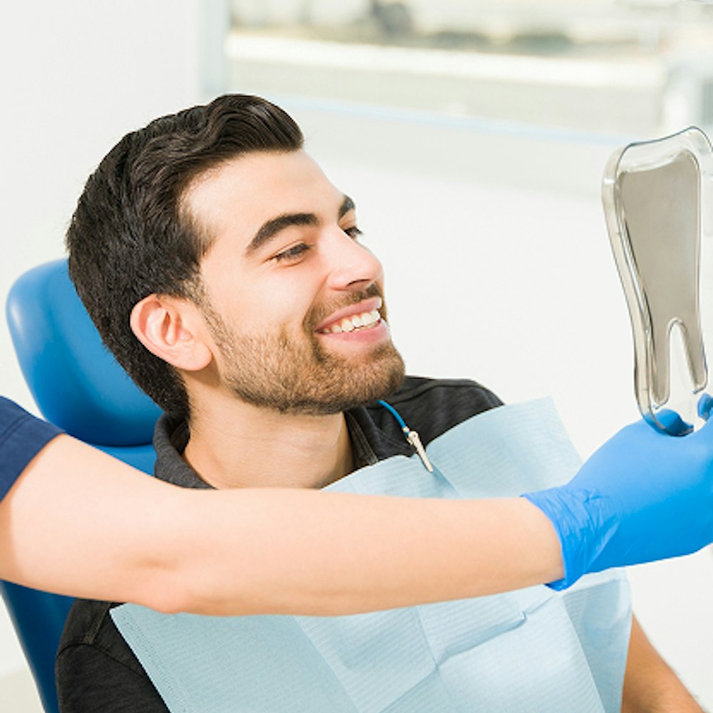 Man smiling in a hand mirror at the dentist