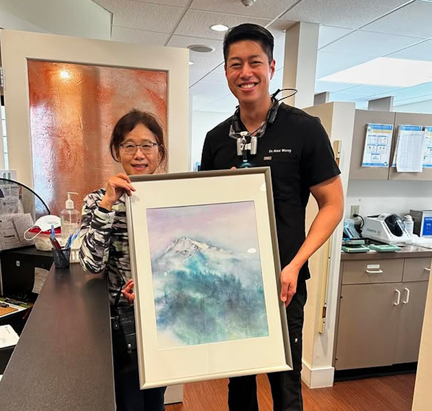 Dr. Alex Wong smiling beside a woman holding a framed picture inside the dental office