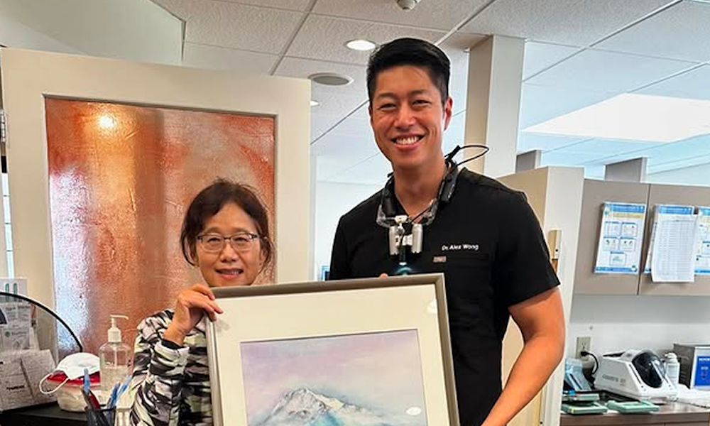 Dr. Alex Wong smiling beside a woman holding a framed picture inside the dental office