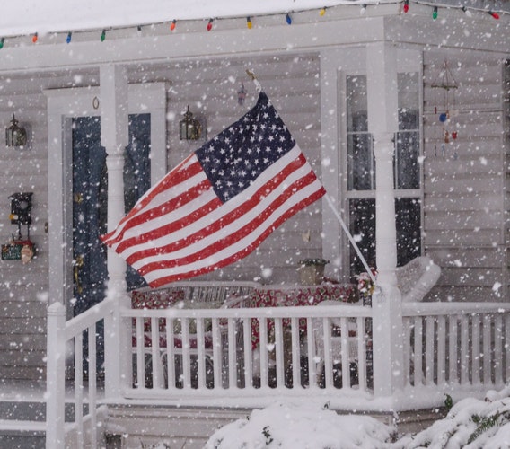 American flag hanging from house porch while snow is falling
