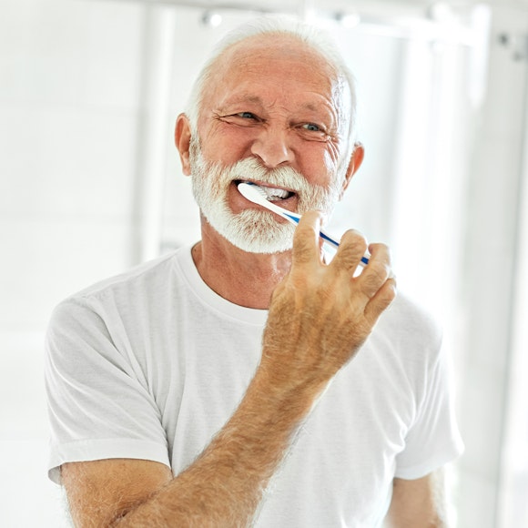 a mature man brushing his implant-supported denture