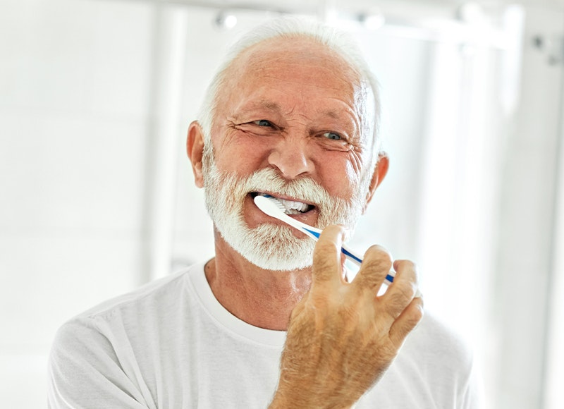 a mature man brushing his implant-supported denture