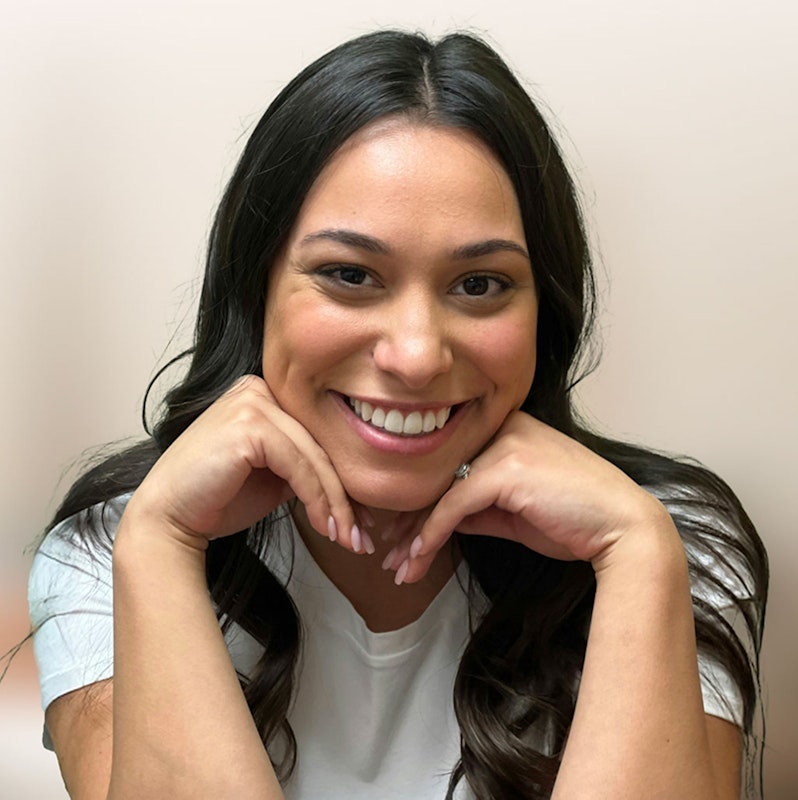 Young woman smiling with hands gently under her chin, highlighting her bright, natural-looking smile