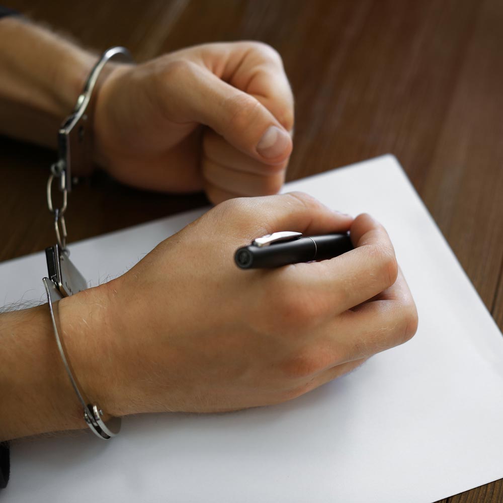 Man in handcuffs signing paperwork