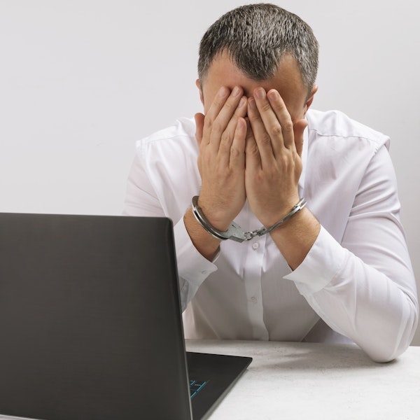 Upset man in handcuffs in front of a computer