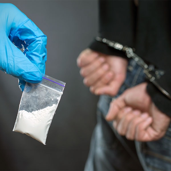 Person in handcuffs while a glove hadn holds a small bag of white powder