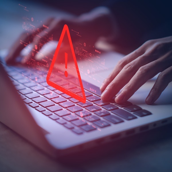 Person typing at computer with red exclamation point 