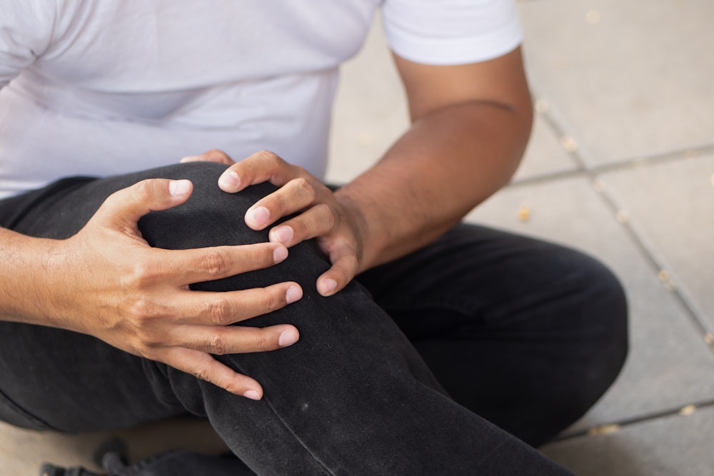 Man sitting on ground, gripping knee in pain
