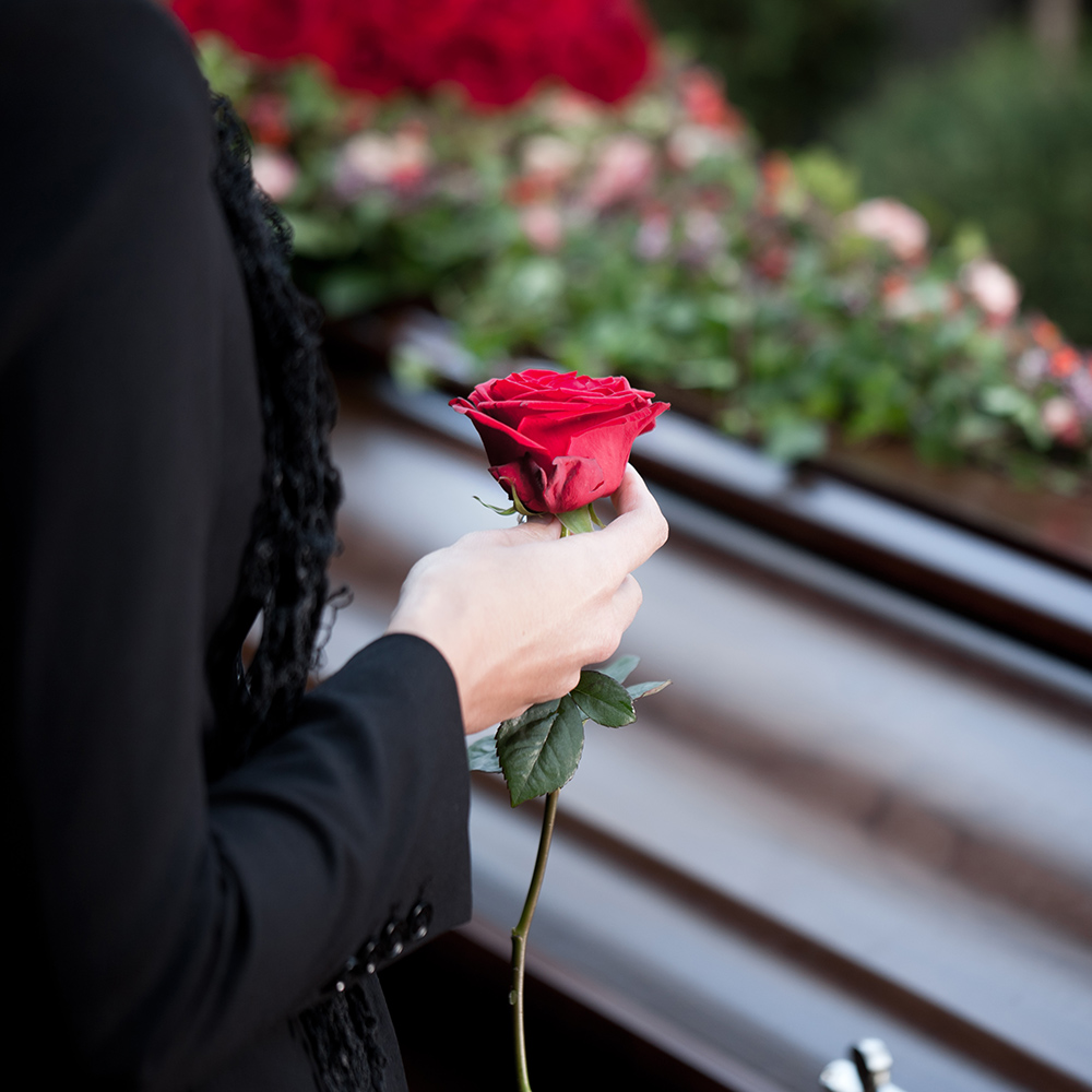 a woman holding a rose next to a coffin