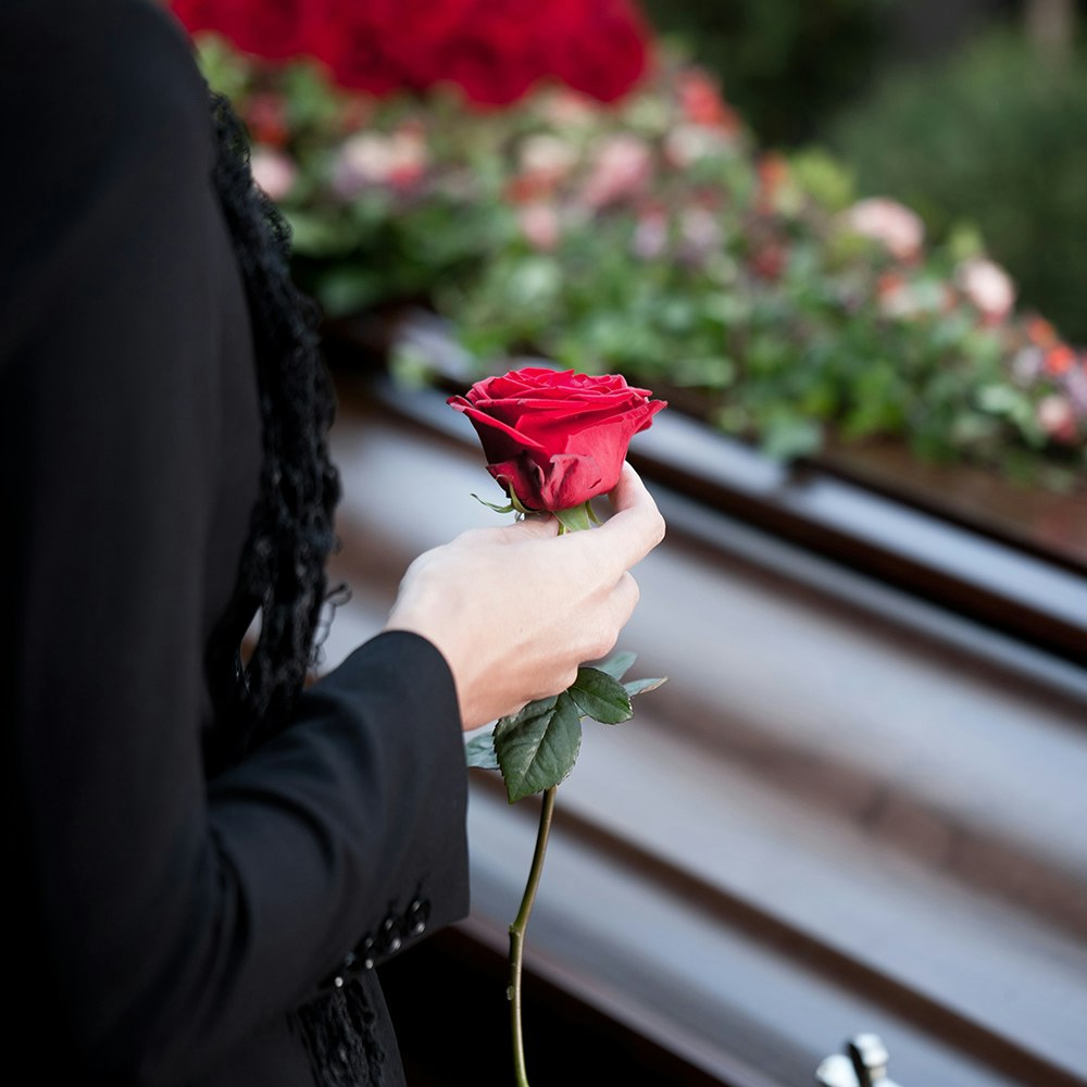 a woman holding a rose next to a coffin