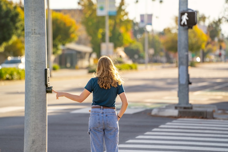 Pedestrian hitting cross button at a crosswalk