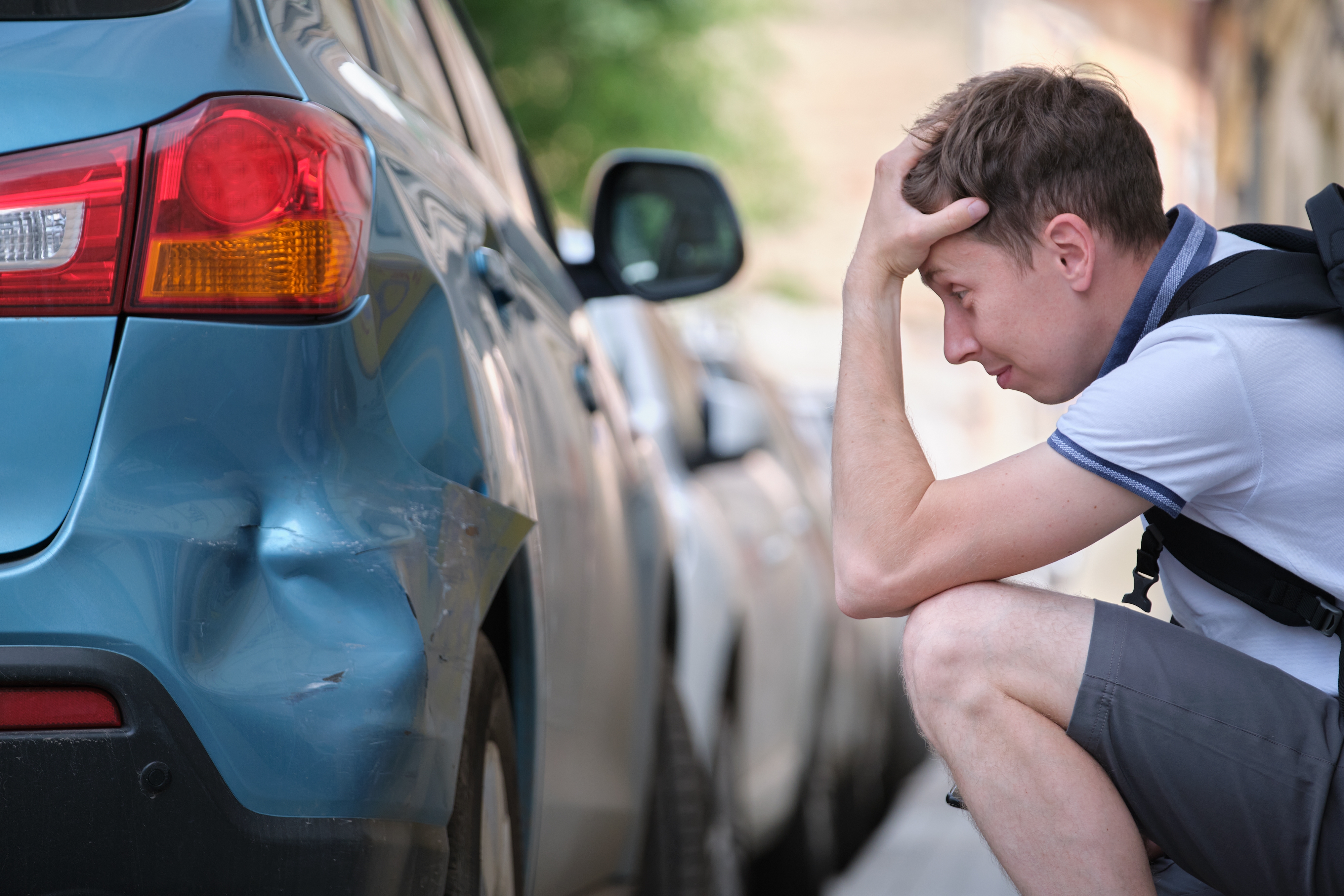 Sad driver looking at car dent