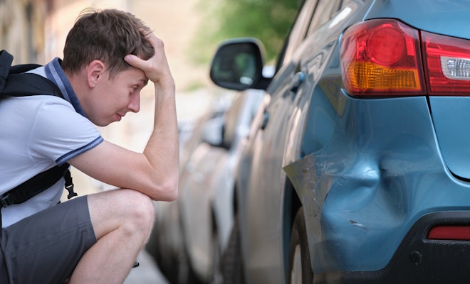 Sad driver looking at car dent