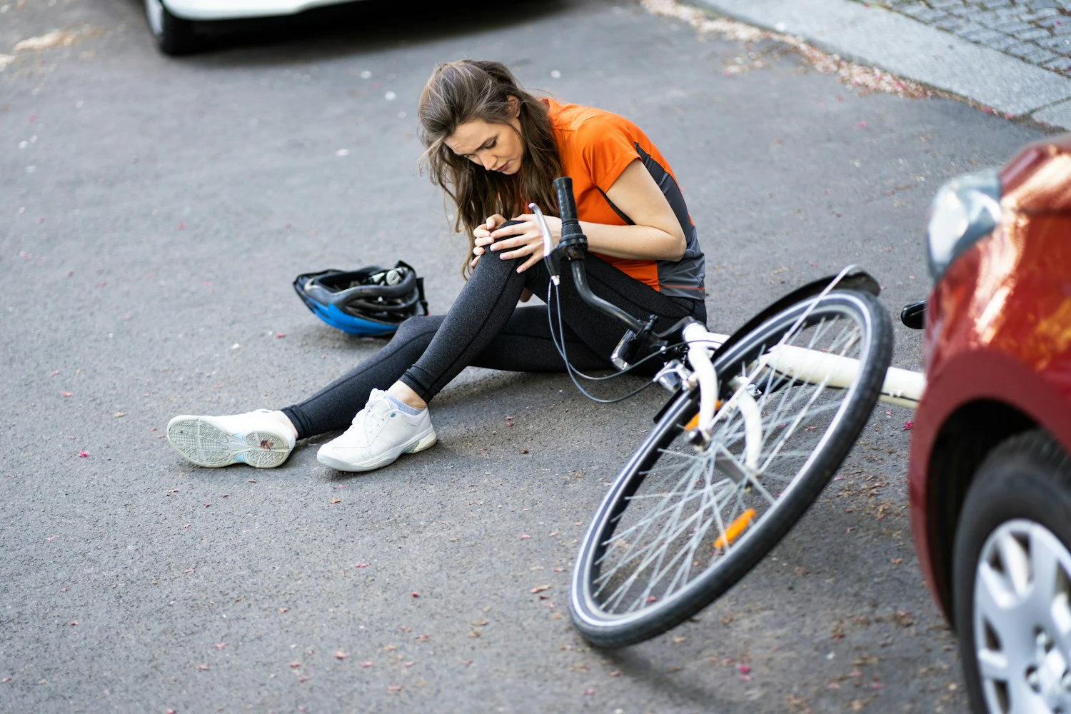 Woman sitting on the road next to a fallen bicycle, injured after being struck by a car