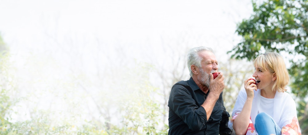 Senior man with dental implants biting into an apple with his daughter