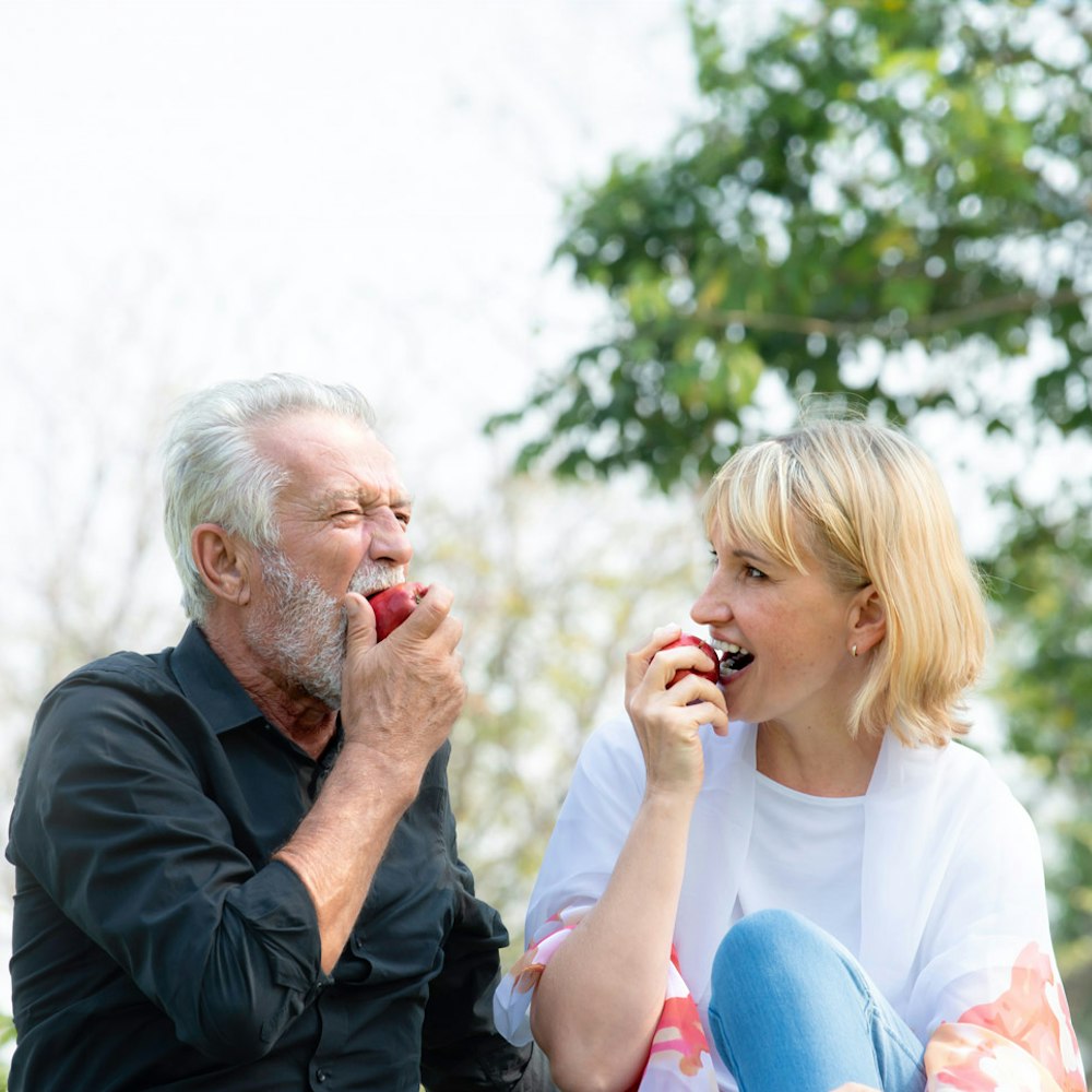 Senior man with dental implants biting into an apple with his daughter