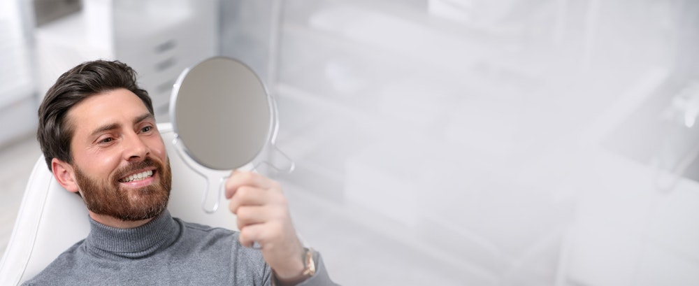 Man smiling in mirror after full mouth reconstruction