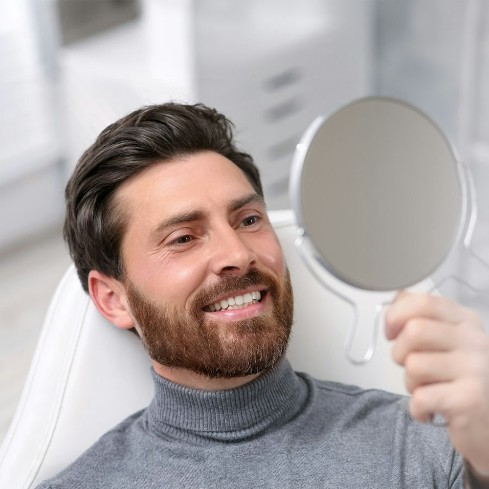 Man smiling in mirror after full mouth reconstruction