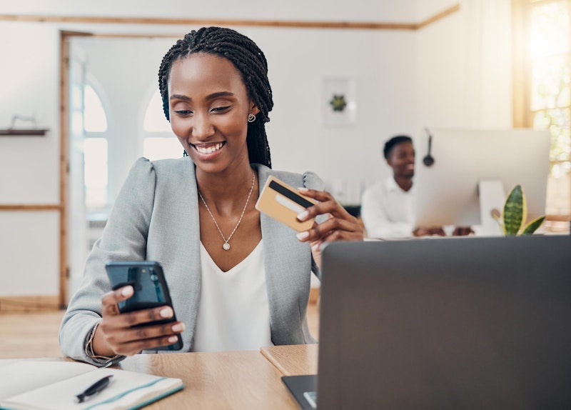 Smiling woman holding credit card and looking at credit score on phone