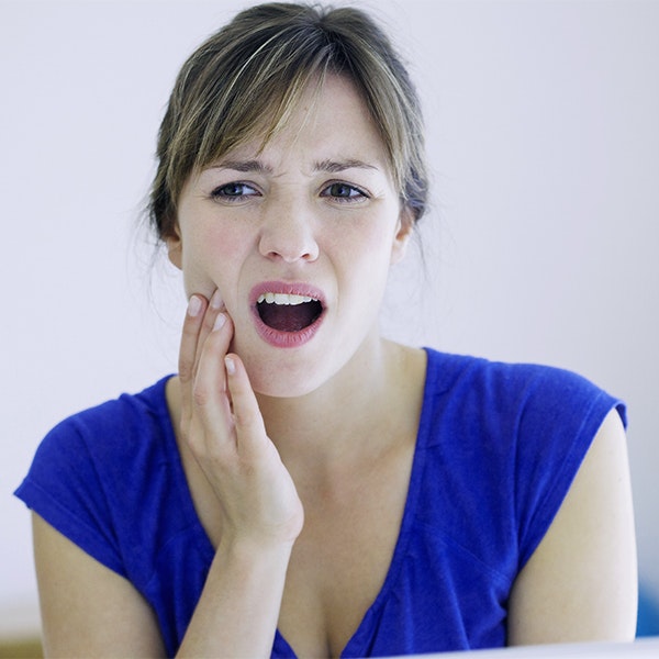 Woman in a blue shirt grasping her jaw in pain