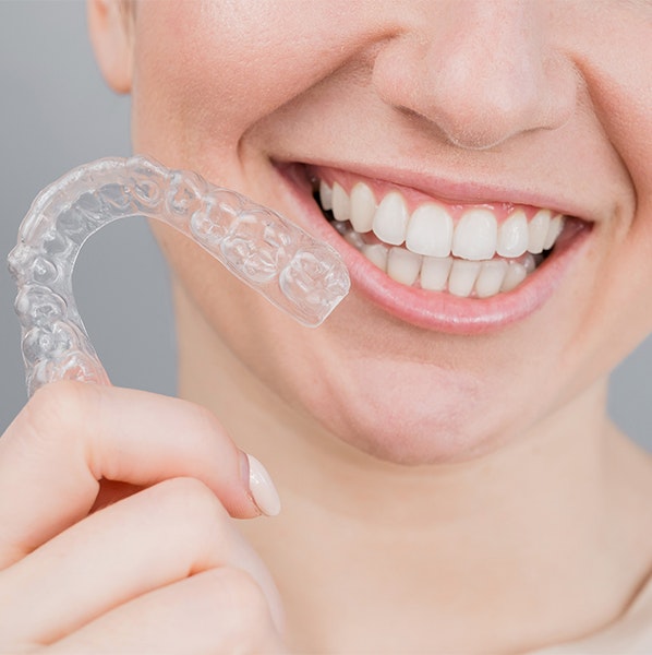 person smiling while holding a clear aligner