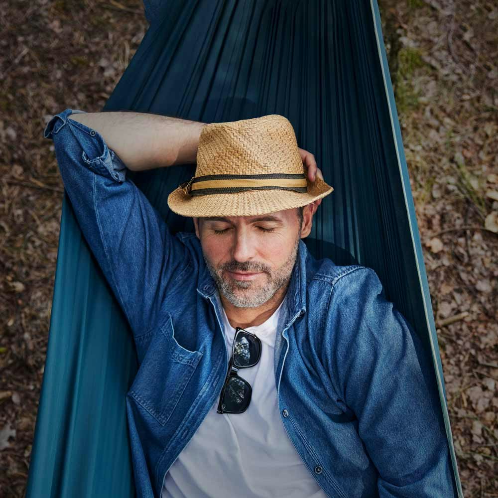 Mature man wearing a hat sleeping in a hammock