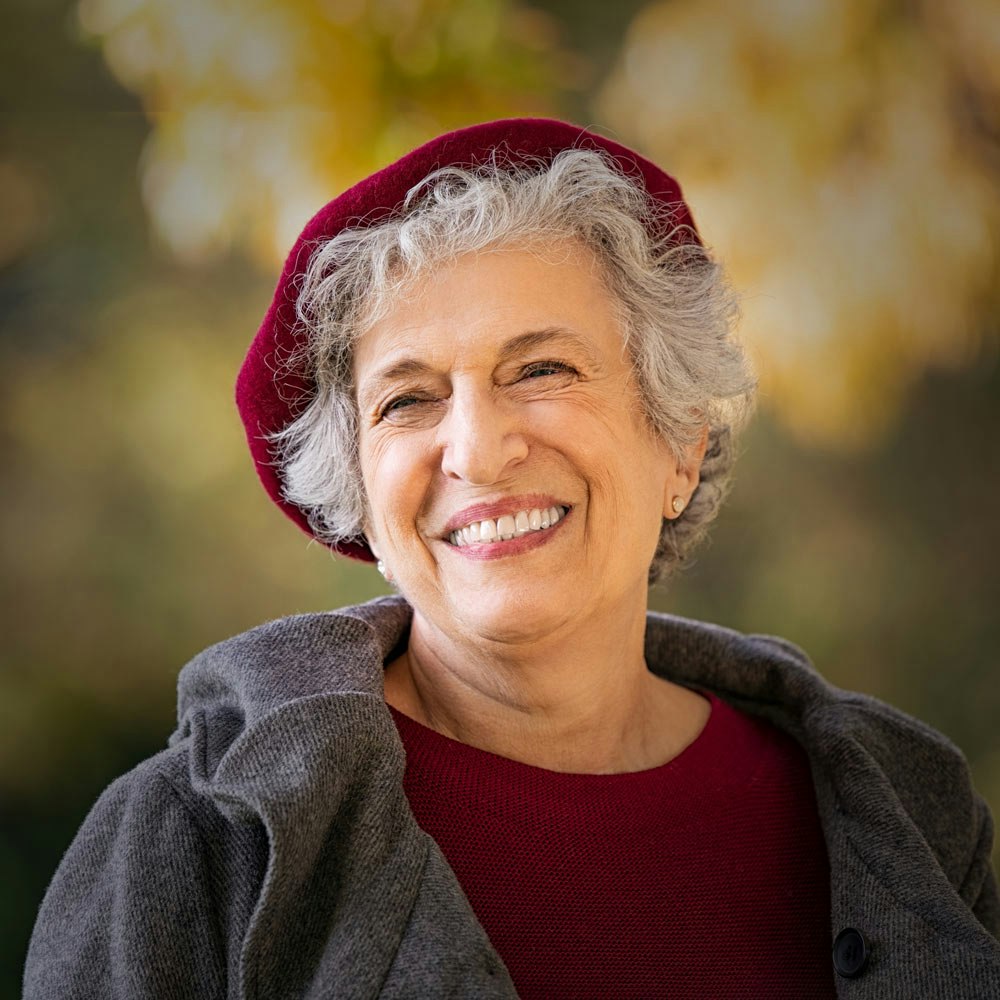 Mature woman with a red cap smiling after dental implants treatment
