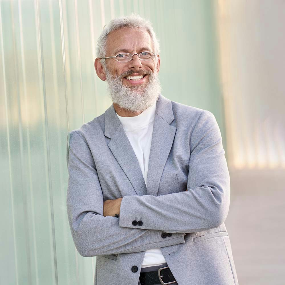 Older man leaning against a wall smiling with a bright, white, straight smile