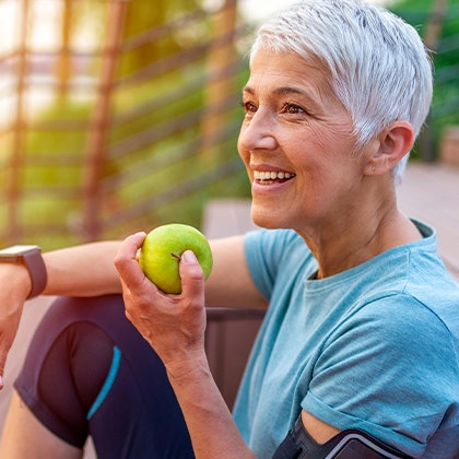 Smiling woman with dental bridge getting ready to bite into an apple