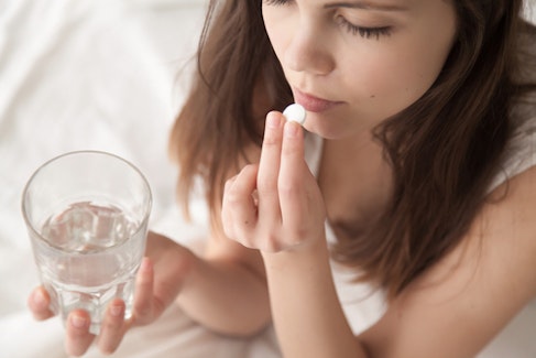young woman taking a pill and holding a glass of water