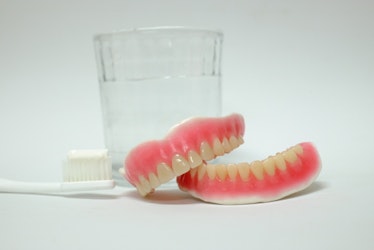 pair of dentures next to glass of water and toothbrush 