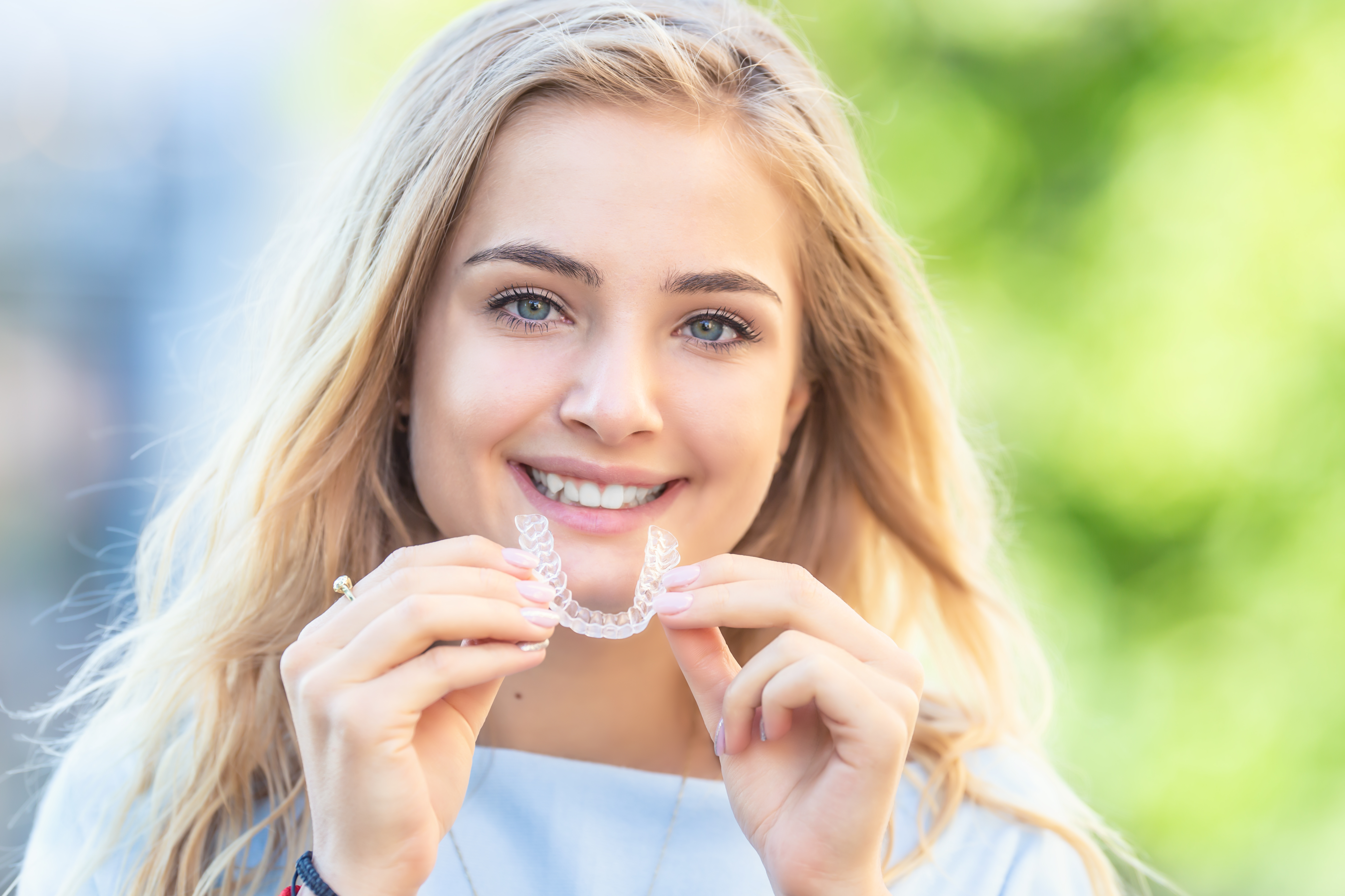 Smiling woman holding clear aligner