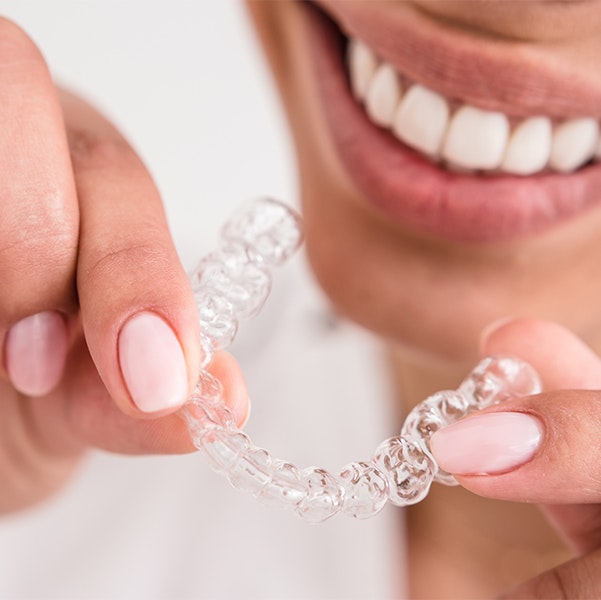 Close up of woman smiling and holding a clear aligner