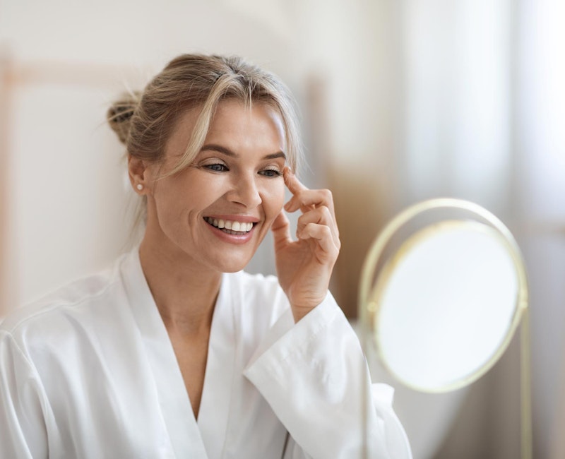 Smiling middle aged woman looking in the mirror at JUVÉDERM results