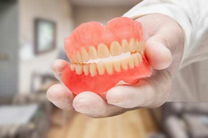 Gloved hand holding a set of traditional dentures