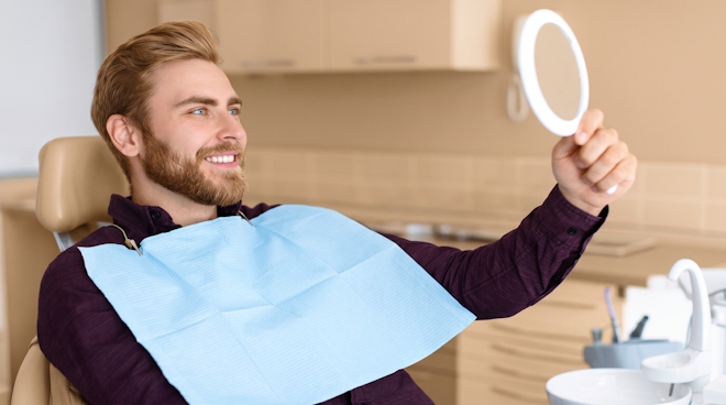 man smiling in mirror at the dentist