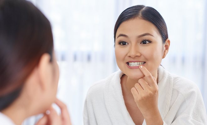 Woman considering gum contouring looking at her smile in the mirror