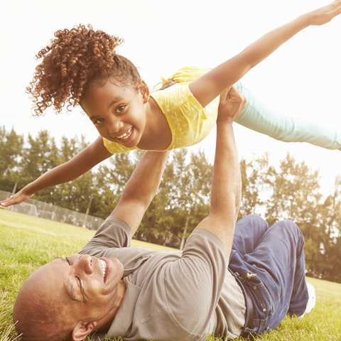 father holding up young girl outside
